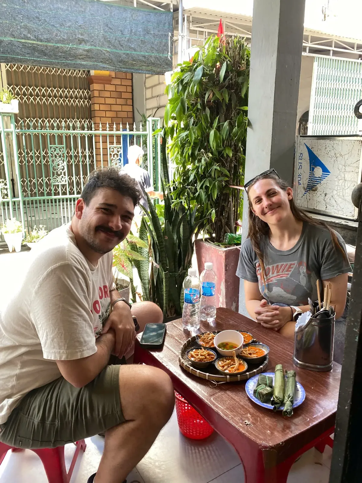 Two travellers at a Da Nang street table with small plates of bánh bèo rice cakes