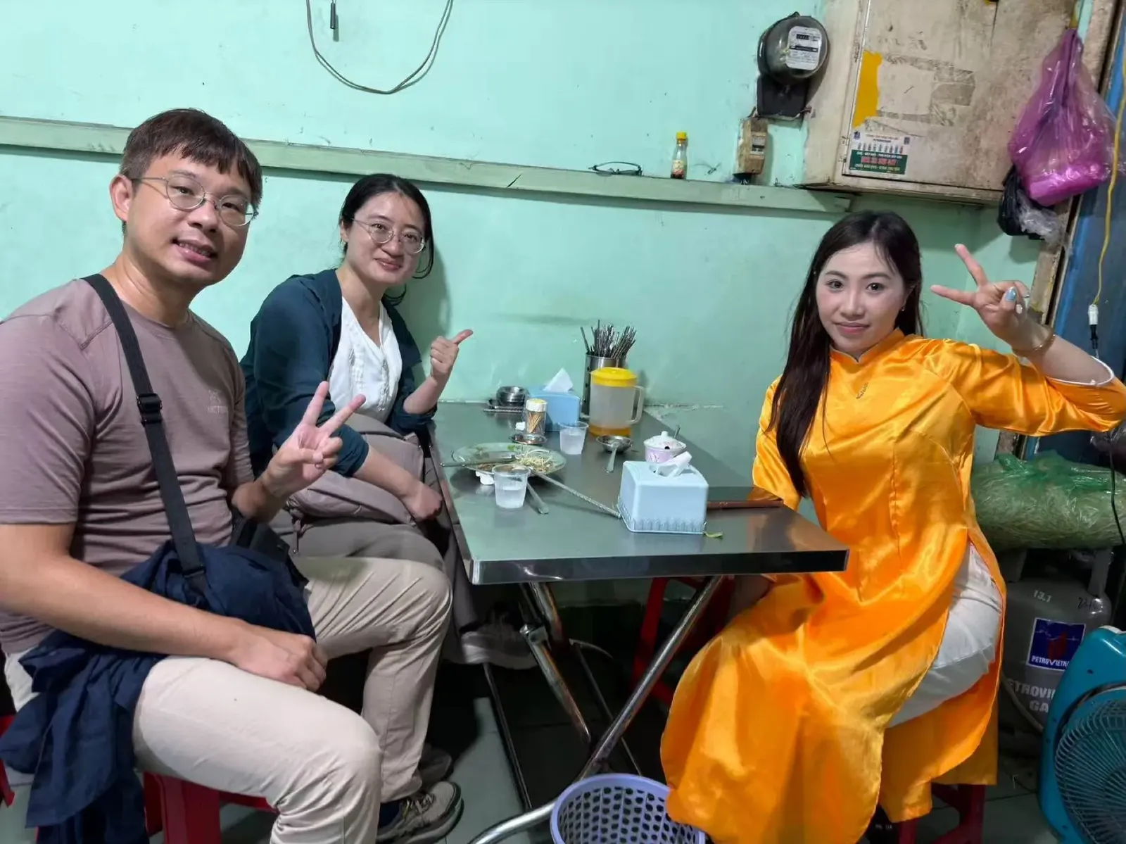 A woman rider in a yellow áo dài sitting with her guests at a local Saigon eatery