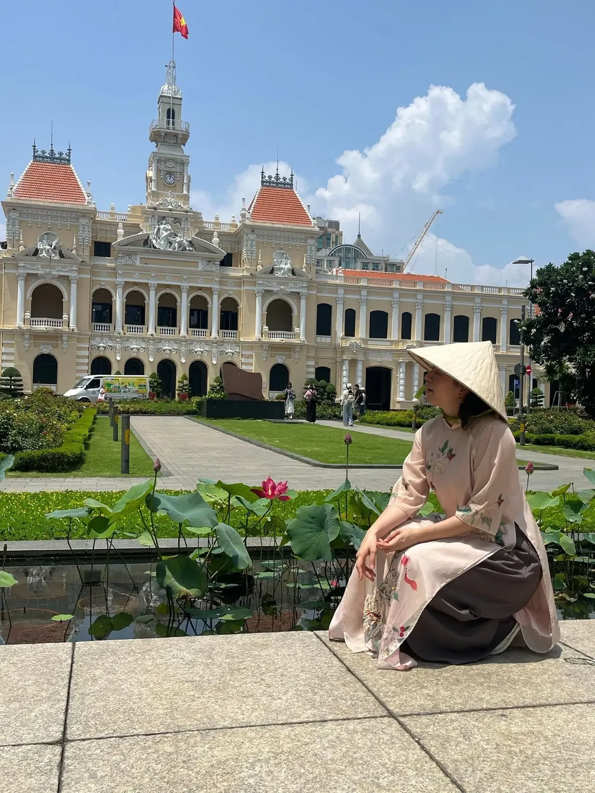 A traveller in a nón lá conical hat sitting in front of Saigon City Hall