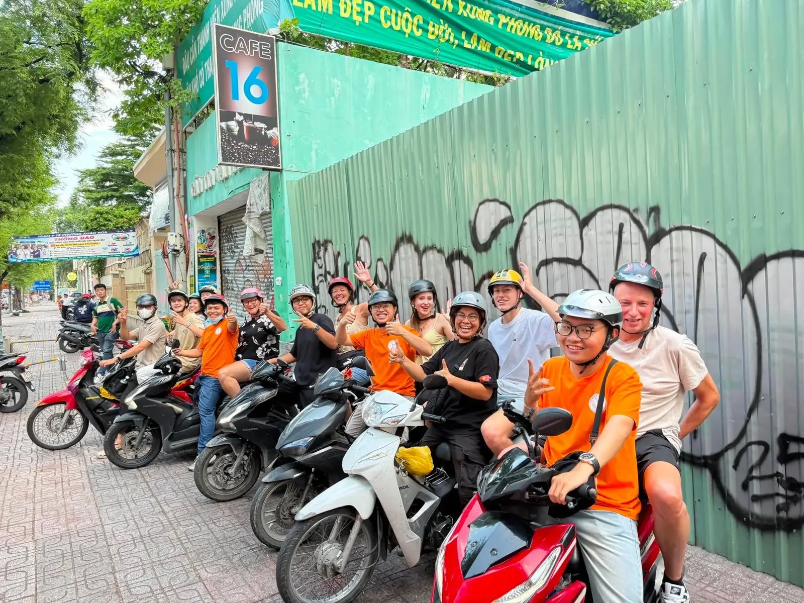 Local riders in orange shirts and their guests lined up on motorbikes before a Saigon street food tour