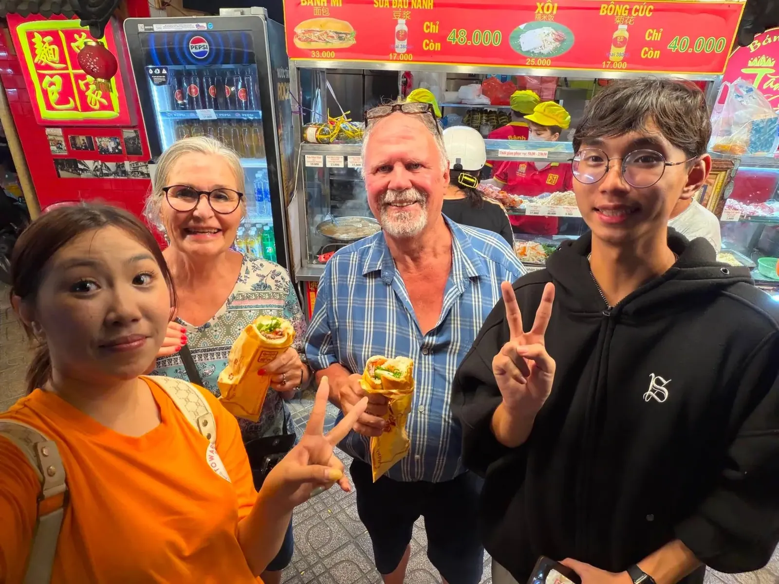 Guests and their guide holding fresh bánh mì at a busy Saigon bánh mì stall