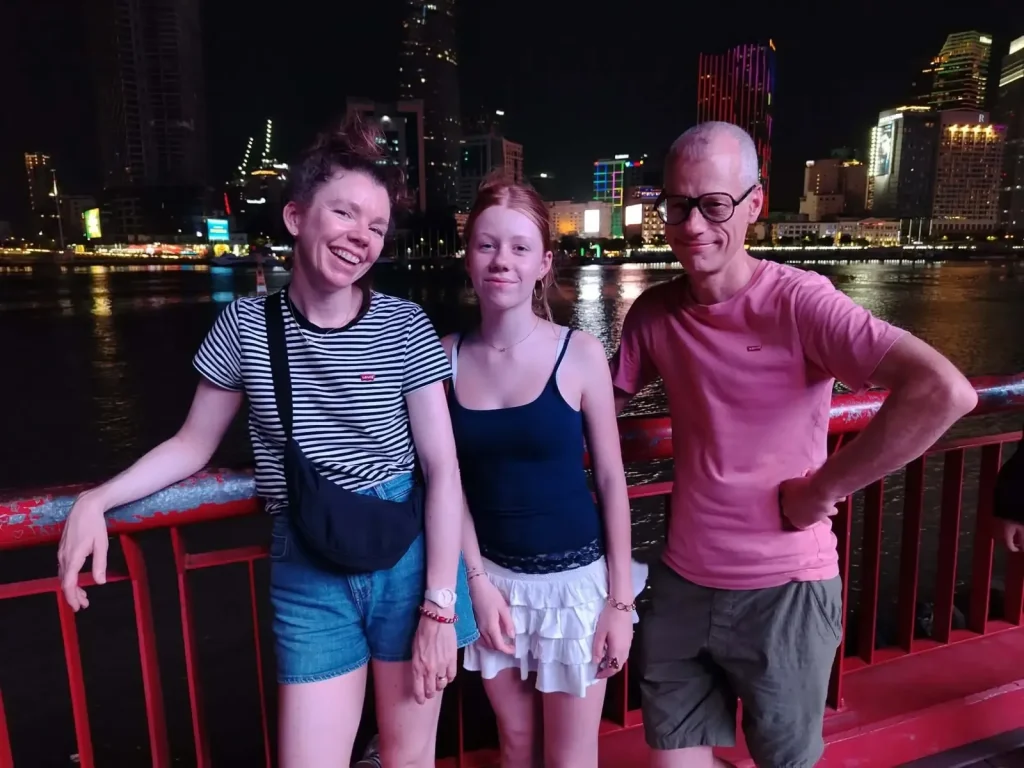 Three guests on the Saigon riverside at night with the lit-up city skyline behind them