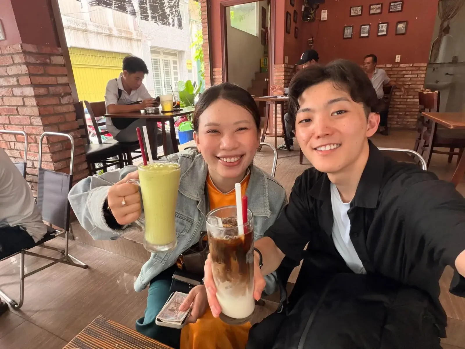 Two guests raising glasses of Vietnamese coffee and a green drink at a Saigon café